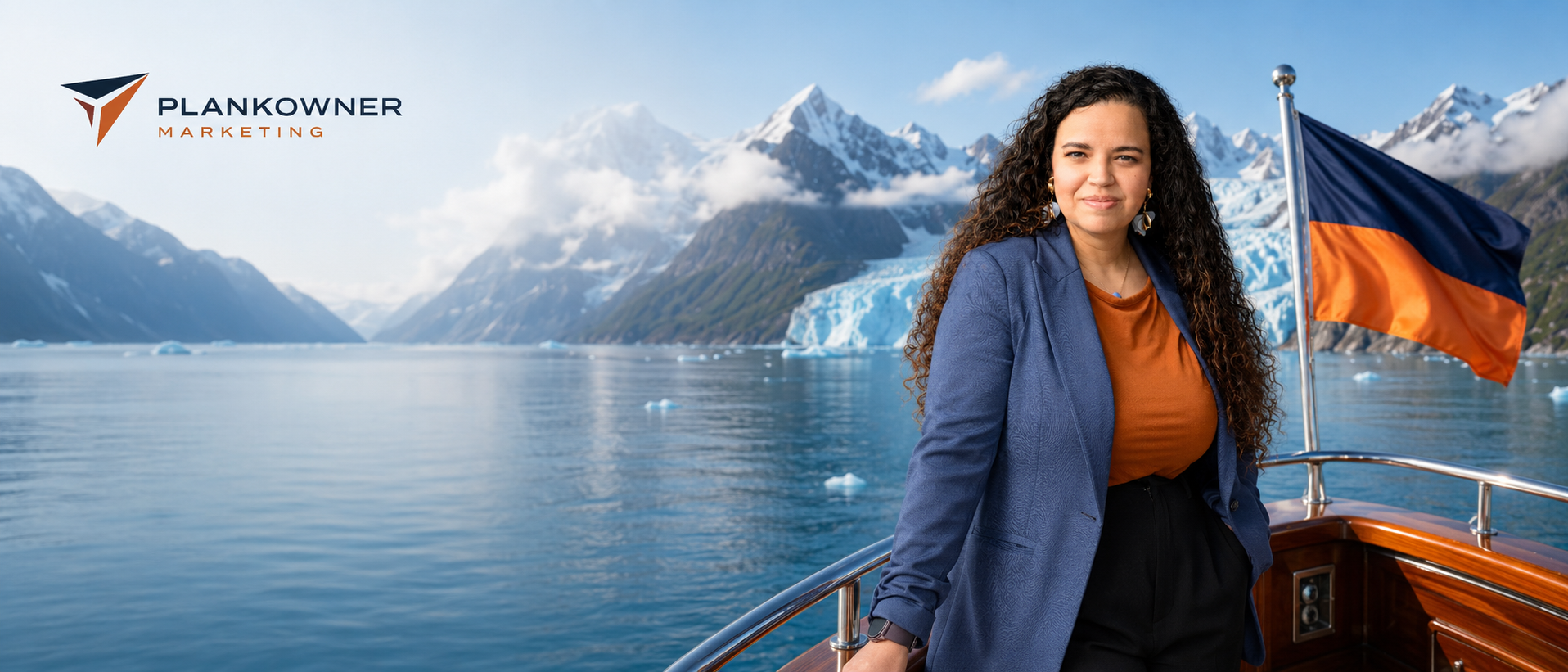 Eve Horne stands on the deck of a wooden boat in a scenic fjord with mountains and glaciers in the background. She is wearing a blue blazer over an orange top.